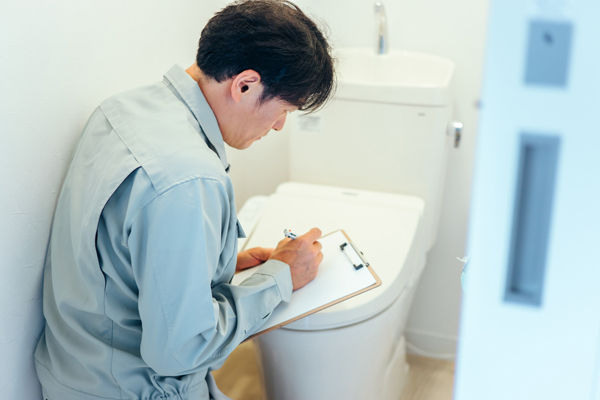 トイレで用紙に記入する作業服の人の画像