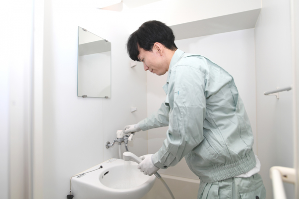 浴室の水栓を触る作業服の人の画像